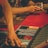 A person reaches into a poker chip case on a red felt table, while another person holds playing cards. The scene is dimly lit, creating a warm and engaged atmosphere.